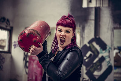 Angry young woman holding metal equipment while standing in abandoned building