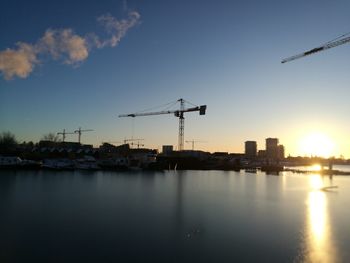 Cranes in city against sky during sunset