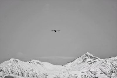 Low angle view of airplane flying over snowcapped caucasus mountains against sky