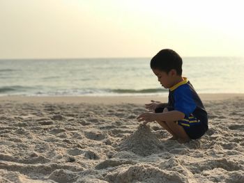 Boy playing with sand at beach against sky