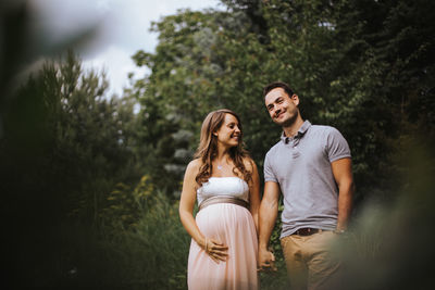 Husband with pregnant wife holding hands in forest