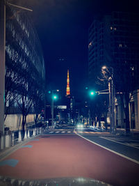 Illuminated street by buildings against sky at night