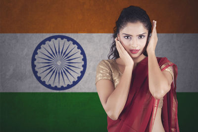 Portrait of woman wearing maroon sari standing against indian flag
