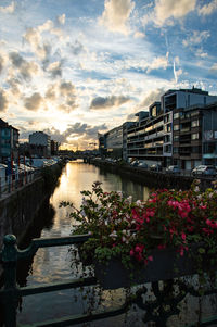 Scenic view of river by buildings against sky during sunset