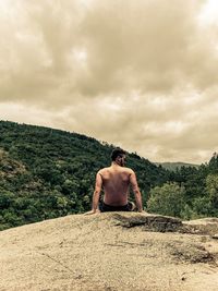 Rear view of shirtless man standing on land against sky