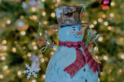 Close-up of snowman against illuminated christmas tree