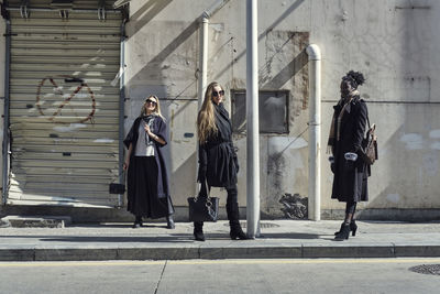 Confident diverse females in trendy wear with accessories standing on pavement near city road