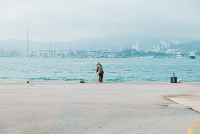 Rear view of man on harbor against sky in city