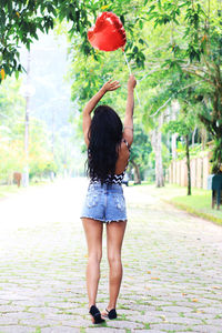 Rear view of woman holding red heart shape balloon while standing on footpath