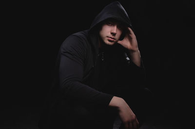 Young man sitting against black background