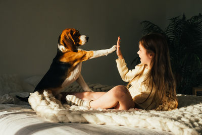 Smiling girl giving high-five to dog on bed at home
