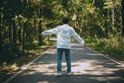 Rear view of man walking on road amidst trees