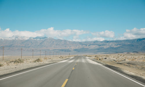 Empty road by mountains against sky