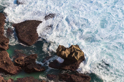 Aerial view of waves splashing on rocks in sea
