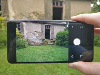 Cropped image of hand photographing abandoned house