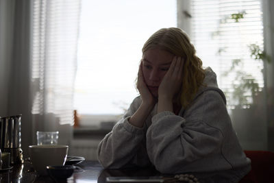 Pensive teenage girl sitting at table with head in hands