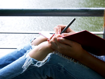 Midsection of woman writing in book while sitting against lake