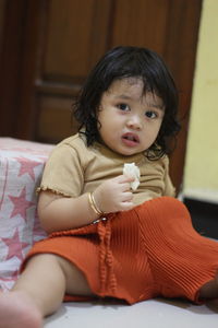 Portrait of cute girl sitting on bed at home