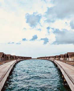 Piers and stilt houses over sea against cloudy sky