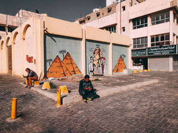 People sitting on street against buildings in city