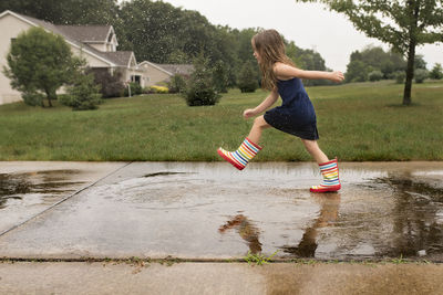 Side view of girl jumping in puddle at footpath