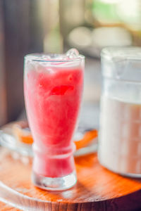 Iced pink milk in glass and glass jug on wood table.