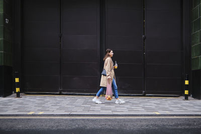 Young woman walking on footpath by black doors