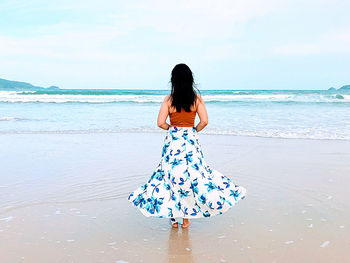 Rear view of woman enjoying at beach against sky