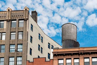 Low angle view of building and factory against cloudy sky