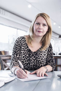 Portrait of businesswoman signing document at restaurant table