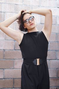 Portrait of young woman standing against brick wall