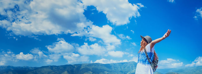 Rear view of man with arms outstretched standing on mountain against sky