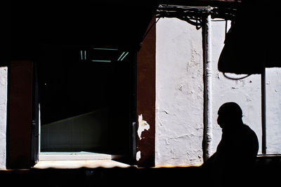 Silhouette man standing by window of abandoned building