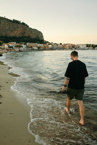 Rear view of man walking on beach against sky