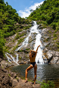 Full length rear view of woman standing against waterfall