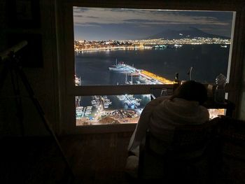 Rear view of man sitting at harbor against sky