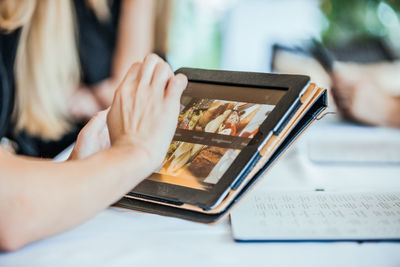 Cropped hand of woman using digital tablet on table