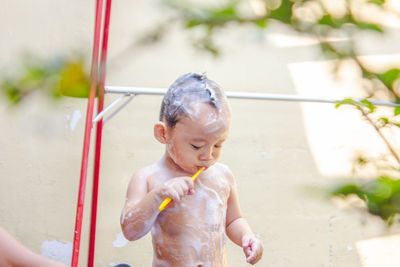 Cute shirtless baby boy with soap sud brushing teeth while standing outdoors