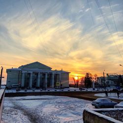 Snow covered buildings against sky during sunset