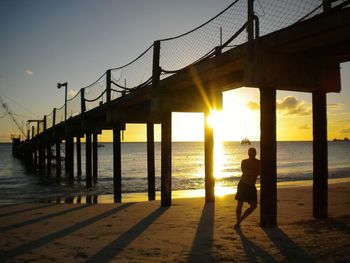 Full length of man standing by pier at beach against clear sky during sunset