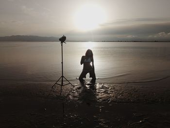 Man photographing at beach against sky during sunset