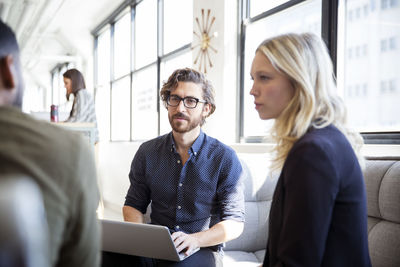 Colleagues discussing while sitting by window in office