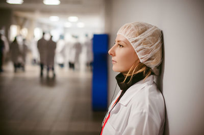 Side view of female doctor wearing surgical cap while standing against wall in hospital