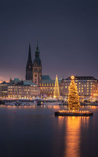 View of illuminated christmas tree in river by buildings in city at night