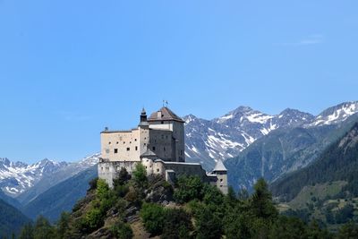 Built structure by trees and mountains against clear blue sky