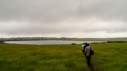 Rear view of friends on grassy field against cloudy sky