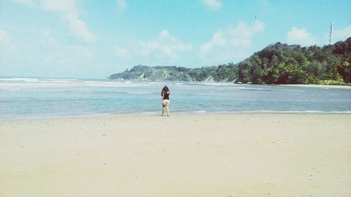 Rear view of woman at beach against sky