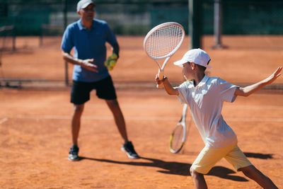 Coach teaching tennis to boy at court