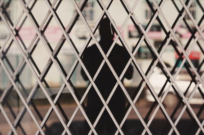 Man reflecting on glass seen through metal grate