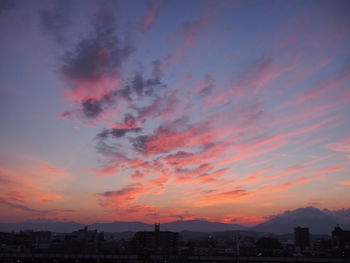 Silhouette of city against cloudy sky during sunset